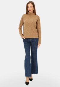 Beżowy sweter dziergany o wysokim dekolcie i wzorze diamentu. Zestawiony z rozszerzanymi niebieskimi dżinsami i czarnymi spiczastymi szpilkami.