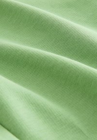 Lichtgroene katoenstof met een gladde textuur, met zachte plooien, die een consistente, zachte afwerking laat zien.