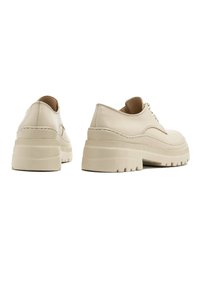 Beżowe buty na platformie z gładką skórzaną cholewką, okrągłym noskiem i zapinaniem na sznurowadła; gruba, fakturowana podeszwa dla stabilności.