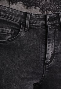 Pantalones vaqueros negros de mezclilla con acabado desgastado, diseño de cinco bolsillos y costuras en contraste. La tela parece suave y duradera con un ajuste estructurado.