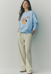 Hellblauer Pullover mit "Limonata" und Zitronengrafik, kombiniert mit cremefarbenen karierter Hosen. Glatter Stoff und lässige Passform.