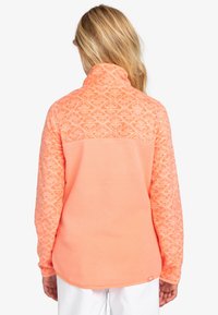 Fleece-Pullover in leuchtendem Korallenrot mit einem gemusterten oberen Abschnitt und einem einfarbigen unteren Teil. Mit hohem Kragen und langen Ärmeln.