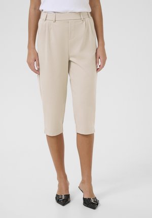 Pantaloni beige cropped con fronte piatto, tasche laterali e risvolti, realizzati in un tessuto liscio. Abbinati a scarpe nere a punta.