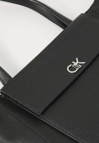 Black leather handbag with a textured surface, featuring a silver logo accent and structured shape. Includes dual shoulder straps.