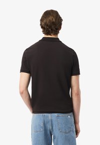 Musta polo-paita, jossa on kauluskot ja lyhyet hihat, yhdistettynä vaaleanssinisiin farkkuihin, joissa on takataskut ja näkyvät ompeleet.