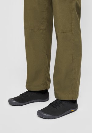 Black athletic shoes with textured gray soles, paired with olive green straight-leg pants featuring a simple design and cuffed hems.