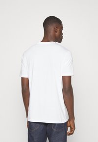 T-shirt en coton blanc avec un col rond, des manches courtes et une coupe décontractée. Présente une texture lisse et aucun motif ou design visible.