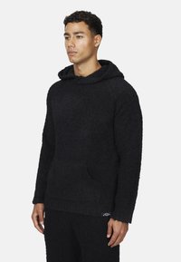 Felpa nera in pile con finitura morbida e testurizzata, dotata di tasca frontale e design del cappuccio rilassato. Etichetta visibile all'orlo.