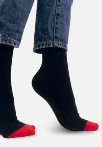 Czarne skarpetki z czerwonymi czubkami, wykonane z gładkiego, elastycznego materiału. Noszone wraz z lekko skróconymi dżinsami.