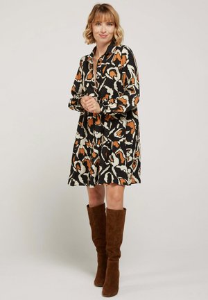 Robe noire avec un motif abstrait orange et crème, manches longues, bouton avant et une silhouette évasée. Bottes en daim marron montantes jusqu'aux genoux.