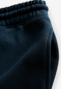 Pantalones de chándal en un azul marino oscuro con una cinturilla elástica acanalada, que exhiben una textura suave y costuras planas. Con bolsillos laterales y un ajuste relajado.