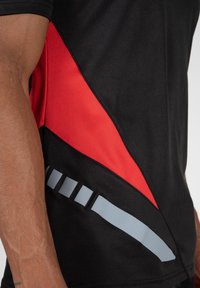Zwarte sportieve T-shirt met een diagonale rode paneel en grijze accenten. Het materiaal is glad en heeft een aansluitend ontwerp, wat de sportieve kleding benadrukt.