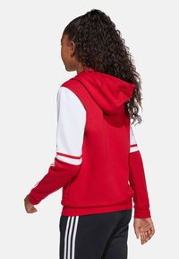 Rode en witte hoodie met een kangoeroezak en een trekkoordkap, voorzien van witte strepen op de mouwen en een ontspannen pasvorm.