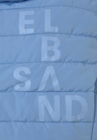 Helle blaue Pufferjacke aus Stoff mit gestepptem Muster und großen, hellen Buchstaben, die "ELBAND" über die Oberfläche schreiben.
