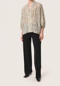 Blusa leggera e stampata in verde pallido e beige, con scollatura a v e vestibilità ampia, abbinata a pantaloni neri a gamba larga e scarpe nere con punta.