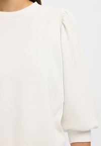 Weißer Pullover mit rundem Ausschnitt, weichem Material und Puffärmeln. Das Design zeichnet sich durch eine lässige Passform und einen minimalistischen Stil aus.