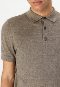 Polo de culoare maronie, cu mânecă scurtă, realizat dintr-un material texturat, având un guler și trei nasturi închisi pe plastron.