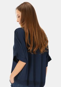 Luźna bluzka w kolorze granatowym, z krótkimi rękawami i prostym dołem. Gładka tekstura z delikatnym połyskiem. Posiada swobodny krój.