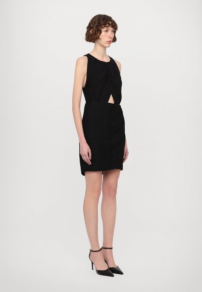Vestido negro sin mangas con un frente retorcido, de longitud a la rodilla, hecho de una tela texturizada. Combinado con tacones negros de tiras.