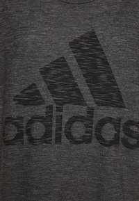 Černé melírované tričko s velkým tmavým logem Adidas na přední straně. Kulatý výstřih a měkká, strukturovaná tkanina.