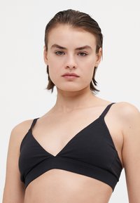 Zwarte katoenen bralette met een V-hals ontwerp, dunne verstelbare bandjes en een zachte textuur. Beschikt over een naadloze uitstraling en een minimalistische stijl.