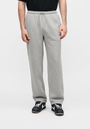 Homme portant un pantalon de jogging gris clair avec taille à cordon et des baskets noires avec lacets blancs et logo Swoosh.