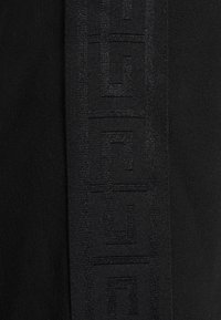 Gros plan d'un tissu noir avec un motif géométrique vertical en relief présentant des formes carrées entrelacées.