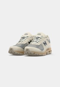 Pair of beige and gray New Balance athletic shoes with white laces, positioned side by side on a white background.