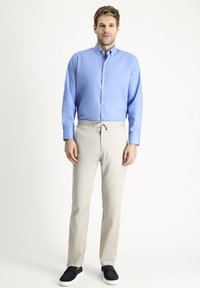 Camisa de botones azul claro, pantalones beige con cordón y zapatos negros sin cordones. Tela suave, corte entallado y estilo casual.