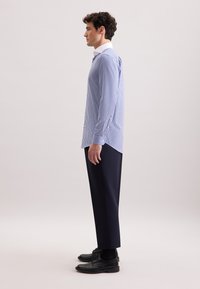 Camicia a righe blu e bianca, maniche lunghe, vestibilità slim, abbinata a pantaloni scuri sartoriali e scarpe nere.