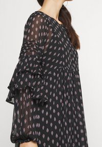 Musta mekko, jossa on kukkakuosi punaisen ja valkoisen sävyissä. Varustettu läpinäkyvällä kankaalla, pitkillä röyhelöhihansuilla ja rennolla istuvuudella.