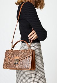 Borsa a tracolla con stampa pitonata marrone, dalla forma strutturata, dotata di manico superiore e tracolla rimovibile. Accentuata da accessori metallici.