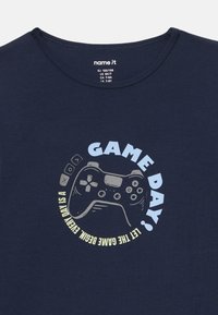 Granatowa koszulka z grafiką szarego kontrolera do gier oraz napisem "DZIEŃ GRY! NIECH GRA SIĘ ZACZNIE - KAŻDY DZIEŃ TO".
