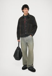 Denim jacket in dark wash, oversized cut, layered over gray graphic tee. Light gray wide-leg jeans, black bag, and embroidered black slippers.