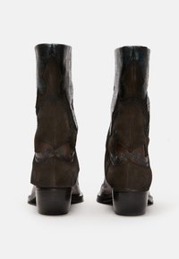 Brown suede ankle boots with a black textured upper, featuring blue stitching and zigzag cutouts. Low heel and smooth black sole.