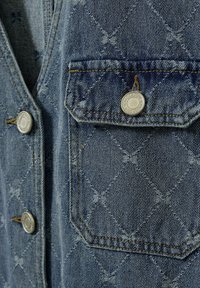 Τσέπη τζιν μπουφάν με καπάκι που ασφαλίζει με μεταλλικό κουμπί, σχέδιο ραφής διαμαντιού και πεταλούδας, και τρία επιπλέον μεταλλικά κουμπιά στο μπροστινό μέρος του μπουφάν.
