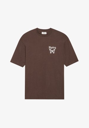 T-shirt marron à manches courtes en coton, avec le texte "Mystère" en blanc et un graphique de papillon sur la poitrine gauche.
