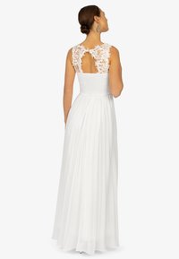 Robe blanche avec un corsage ajusté ornée de dentelle et un dos à découpe en forme de clé, jupe plissée fluide en tissu léger.