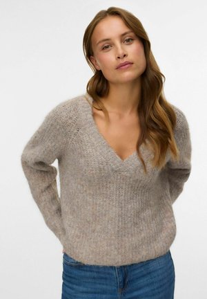 Licht beige gebreide trui met een v-hals, lange mouwen en een gestructureerde afwerking. Gecombineerd met blauwe denim jeans.