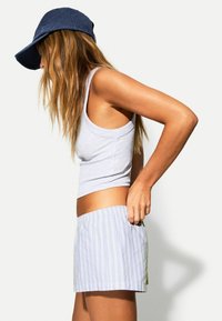 Canotta grigia chiara e pantaloni a strisce, con motivi blu e verdi. I pantaloni hanno una vita elastica e tasche.