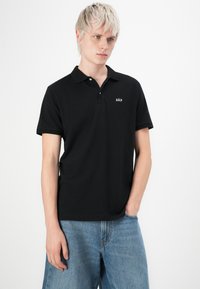 Un polo noir en coton avec un col, des manches courtes et un petit logo "GAP" blanc sur la poitrine gauche. Assorti avec un denim bleu clair.