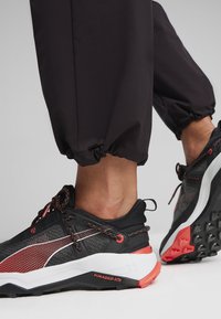 Scarpe da ginnastica nere e grigie con tomaia testurizzata, dettagli arancioni e particolari riflettenti. Suola resistente con modelli di trazione.