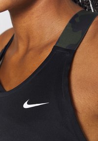 Gros plan d'une personne portant un haut de sport Nike noir avec un logo blanc et une bretelle à motif camouflage.