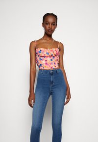 Top floral em rosa com realces em azul e roxo, apresentando um decote pregueado. Usado com calças de ganga de cintura alta em azul.