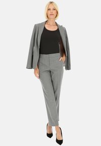 Szary, dopasowany garnitur z elegancką marynarką i prostymi spodniami. Czarna bluzka pod spodem, w komplecie z czarnymi szpilkami. Gładki materiał i czyste linie.