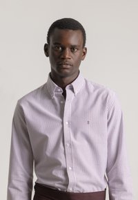 Camisa de botón con rayas verticales moradas y blancas, hecha de una tela ligera. Cuenta con un cuello estilo spread y un logotipo bordado en el pecho.