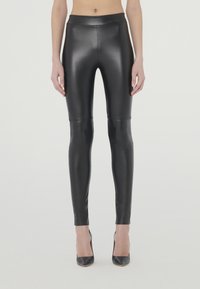 Zwarte nepleer leggings met een gladde, glanzende textuur, hoge tailleband en een aansluitende silhoët, gecombineerd met zwarte hoge hakken.