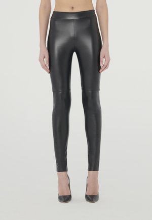 Zwarte nepleer leggings met een gladde, glanzende textuur, hoge tailleband en een aansluitende silhoët, gecombineerd met zwarte hoge hakken.