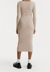 Abito midi a maglia a coste in beige chiaro, con maniche lunghe, silhouette aderente e scollo rotondo; abbinato a scarpe con tacco alto nere e calzini bianchi.