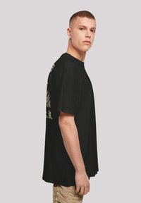 Černé bavlněné tričko s volným střihem, se světle krémovým grafickým designem na zadní straně a kulatým výstřihem.